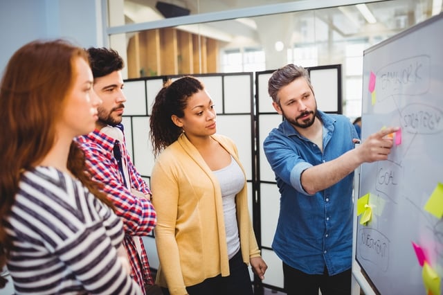 Executive explaining strategy to colleagues on whiteboard in creative office.jpeg